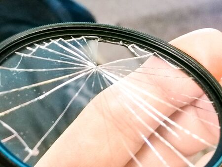 A photography lens filter that has been smashed but still remains inside the metal frame.