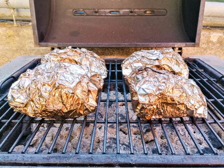 A small barbeque that has been prepared with hot coals and on top jacket potatoes are wrapped for...