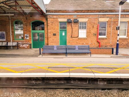 A view along a British train station platform during a sunny day. Multiple posts hold up the long platform shelter.の写真素材