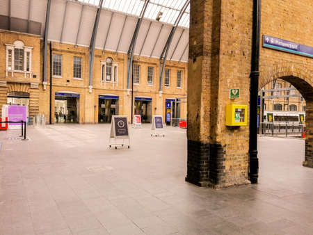 A view along a British train station platform during a sunny day. Multiple posts hold up the long...