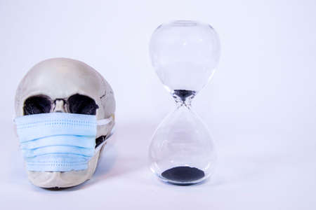 A human skull sits next to a glass timer that is counting down to disaster. During the pandemic of the virus.の写真素材