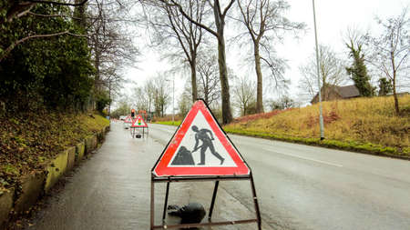Roadworks being carried out on a steep incline of road. Signs and control measures in place to keep control of the traffic going up and down the road.の写真素材