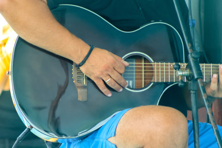 A black acoustic guitar being played by a person on a bar stool.