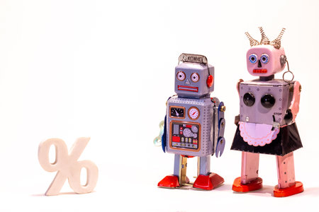 Two robot people stand side by side with an interest rates / percentage sign close by, against a...