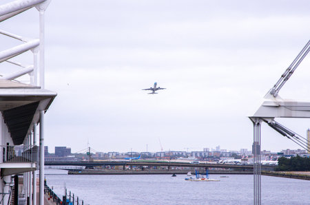 A large commercial aircraft taking off from London City Airport, in the United Kingdom, flying over the Royal Victoria Dock.の写真素材