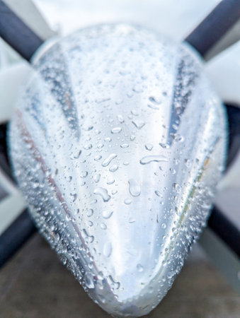 A very shiny, new, chrome spinner on the front of an aircraft's engine. Covered in rain drops.の写真素材