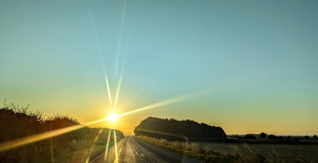 Awe inspiring colours as the sun goes down behind a lovely landscape, seen from a country road,...