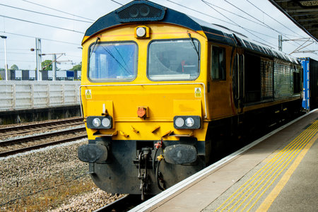 A very powerful freight train pulling it's loaded carriages past a station platform, in the United Kingdom.の写真素材