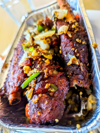 Delicious Chinese takeaway spare ribs, covered in herbs and sauce placed in a foil tub ready for consumption.の写真素材