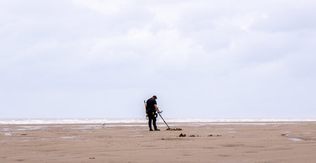 An adult male walking along the beach with a metal detector to seek our treasures hidden below the surface.の写真素材