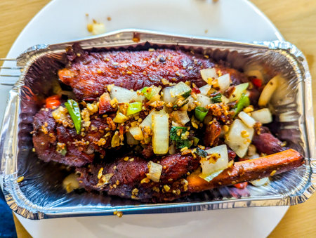 Delicious Chinese takeaway spare ribs, covered in herbs and sauce placed in a foil tub ready for consumption.の写真素材
