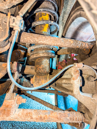 The underbody of a vehicle that is a little rusty, with a close up view of the suspension that enables the car to have a smoother ride.の写真素材
