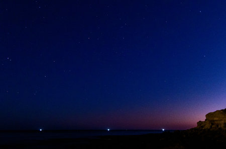 A beautiful night beach setting with the colourful skies and stars over the seafront of a coastline.