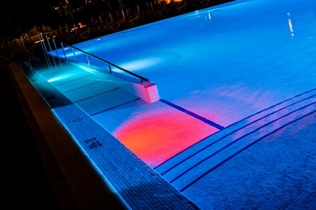 A night view of a hotel or resort swimming pool during the dark with the pool illuminated by underwater lights.の写真素材