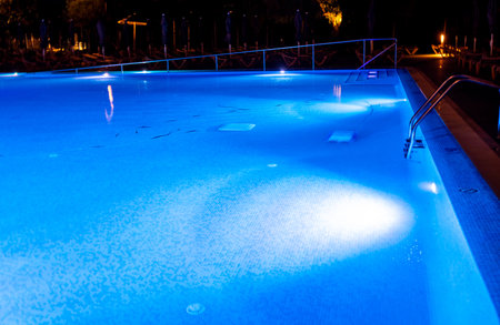 A night view of a hotel or resort swimming pool during the dark with the pool illuminated by underwater lights.の写真素材