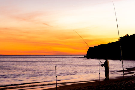 A relaxing sport, fishing on a European beach, at night when the sun is setting. Rods set up with the lines in the open calm sea.の写真素材