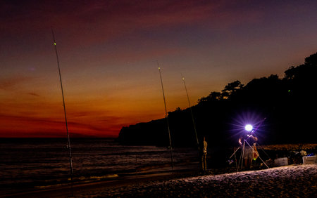 A relaxing sport, fishing on a beach, at night when the sun is setting. Rods set up with the lines in the open calm sea.の写真素材