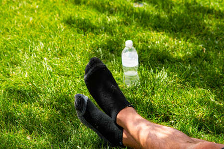 Man laying on cool grass in park enjoying warm summer day with bottle of water nearby.