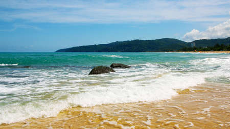 Boulders, the surf, and the blue sky over the sea, Karon sandy beach on a sunny day, Thailandの写真素材