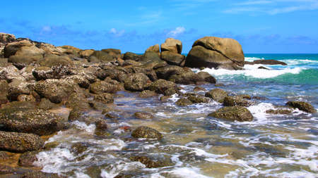Boulders, the surf, and the blue sky over the sea, Karon sandy beach on a sunny day, Thailand
