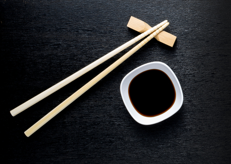 Japanese sushi chopsticks over soy sauce bowl, rice on black backgroundの写真素材