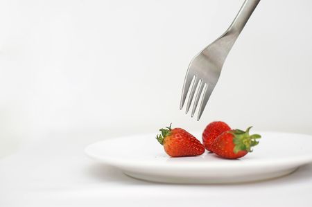 Strawberries and silver fork on white plateの写真素材