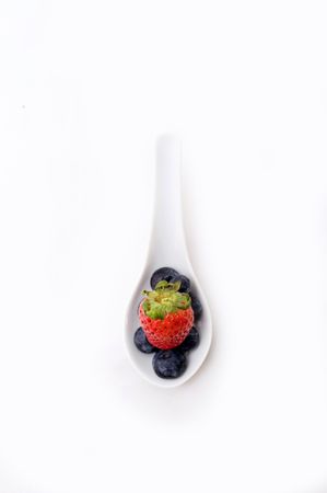 Red strawberry sitting on blueberries in a white spoonの写真素材