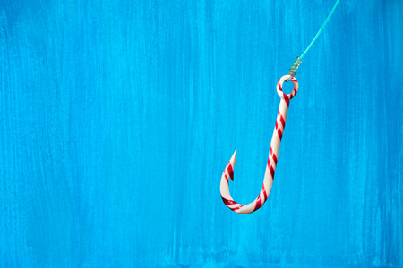 Hooked on sugar. Hook-shaped candy cane with fishing line over blue painted background.の写真素材