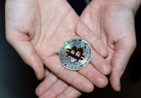 A Bitcoin silver- gold coin in hands.