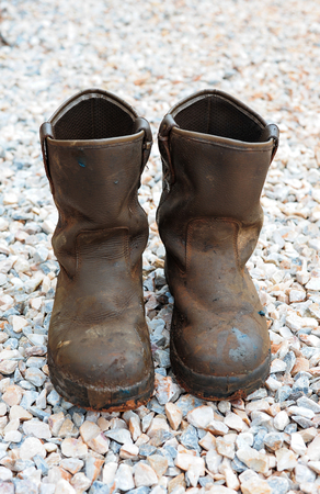 old dirty boots.old boots worn with scratches and untied shoelaces on rock backgroundの写真素材