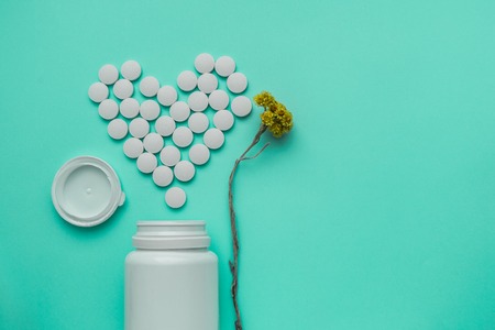 Medicines white, round heart shaped pills isolated on turquoise background.