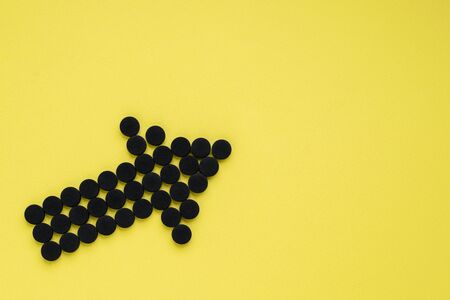 Medical activated carbon in the form of an arrow on a yellow background. Top view, copy space.の写真素材
