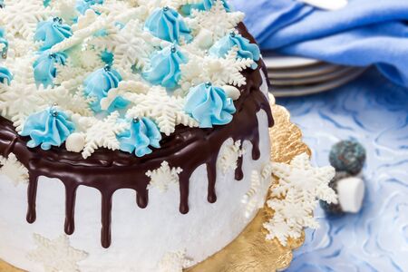 Beautiful half cream cake decorated with chocolate leaks, cream and sugar snowflakes from mastic, on the background of platesの写真素材