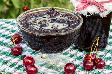 Glass bowl with cherry jam on a background of scattered cherries and cherry jam jarの写真素材