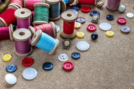 sewing tools (many different colorful thread, needle, many different buttons) on wooden backgroundの写真素材