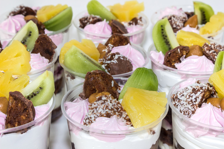 Trifle (cake in glass), chocolate biscuit cakes with cream cheese and blueberry jam, decorated with meringue, fruit (kiwi and pineapple) and candyの写真素材