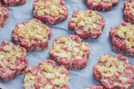 raw fresh pork cutlets with fried onions in the shape of a flower on parchment paperの写真素材