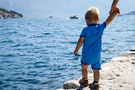 One year old child stands on the edge of the pier and looks at the Bay of Kotor in Montenegro, view from the back.の写真素材