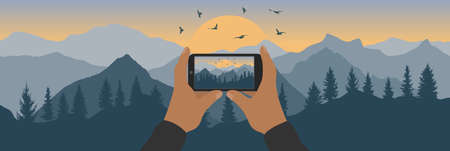 Human hand holding phone and taking photo of silhouette of sunrise in mountains with forest and...