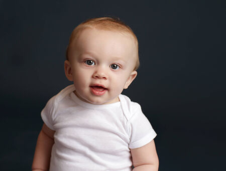 Happy baby laughing and smiling, sitting on a white blanket, dark blue studio backdropの写真素材