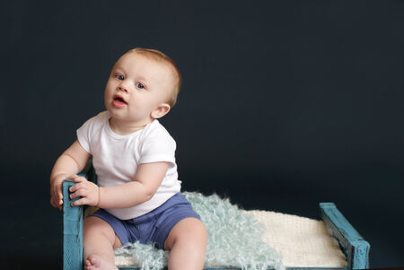 Happy baby laughing and smiling, sitting on a white blanket, dark blue studio backdropの写真素材