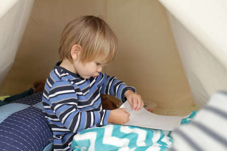 Child playing at home in a tent, drawing and art activity, showing a blank pageの写真素材