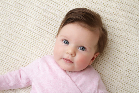 Newborn baby girl posed in a bowl on her back, on knit blanket, smiling looking at camera