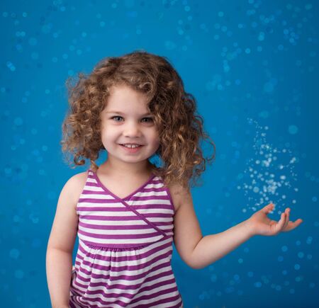 Happy smiling laughing child looking at camera: girl with curly hair against blue background with ice, frozen snowflakesの写真素材