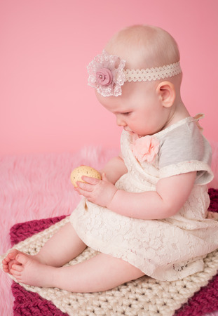 Baby girl on pink background holding an easter eggの写真素材