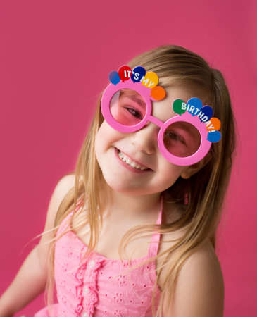 Happy smiling girl in "Happy Birthday" pink sunglasses laughing and looking at the cameraの写真素材