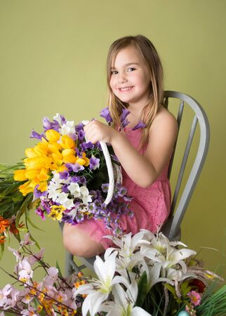 Happy smiling girl with a bunch of spring flowers in a basket looking at the camera, green backgroundの写真素材