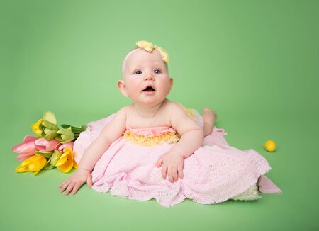 Baby in Easter outfit on her tummy, easter egg and flowersの写真素材