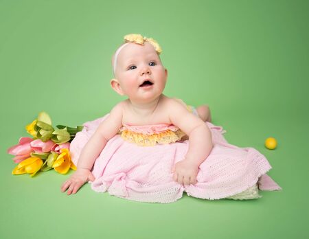 Baby in Easter outfit on her tummy, easter egg and flowersの写真素材