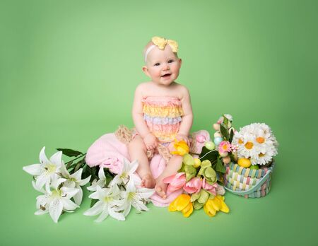 Baby girl in Easter outfit with Easter Eggs, and tulip flowers, sitting on blanketの写真素材